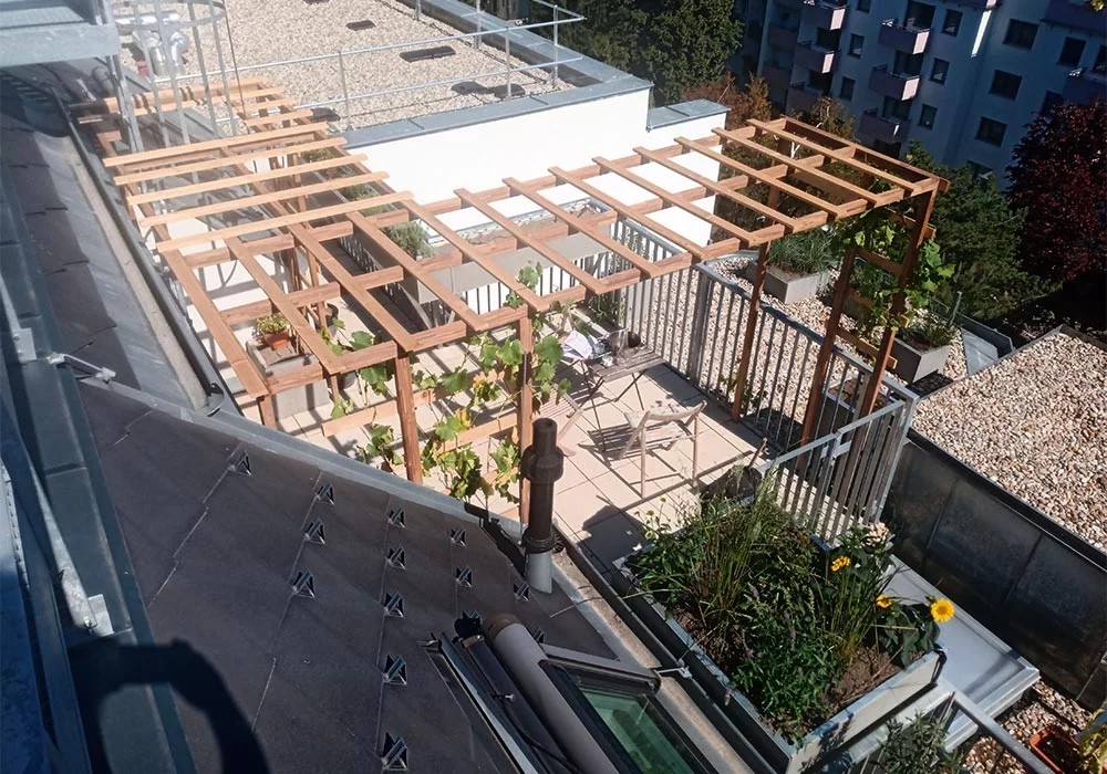 Obenansicht einer kleinen Dachterrasse in Wien. Man sieht eine Holzkonstruktion, auf der Weinreben wachsen werden, damit es auf der Terrasse mehr Schatten gibt.