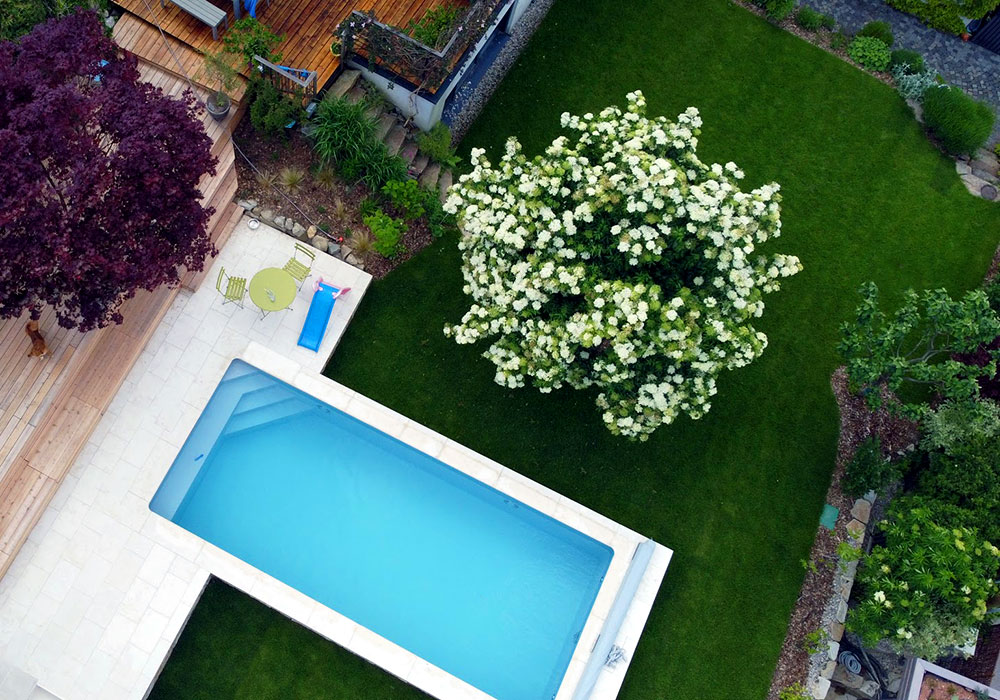 Eine Luftaufnahme zeigt einen großen Garten in Hanglage mit einem Pool und einer Holzterrasse.