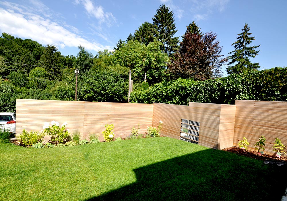 Detailansicht eines Gartens mit grünem Rasen. Im Hintergrund sieht man eine Sichtschutzwand aus Holz. Vor der Wand sind Pflanzen eingepflanzt.