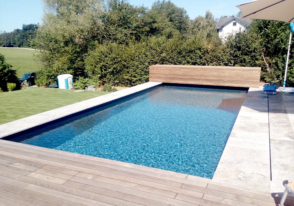 Swimming Pool im Garten mit einer Holzterrasse und einer Steinterrasse.