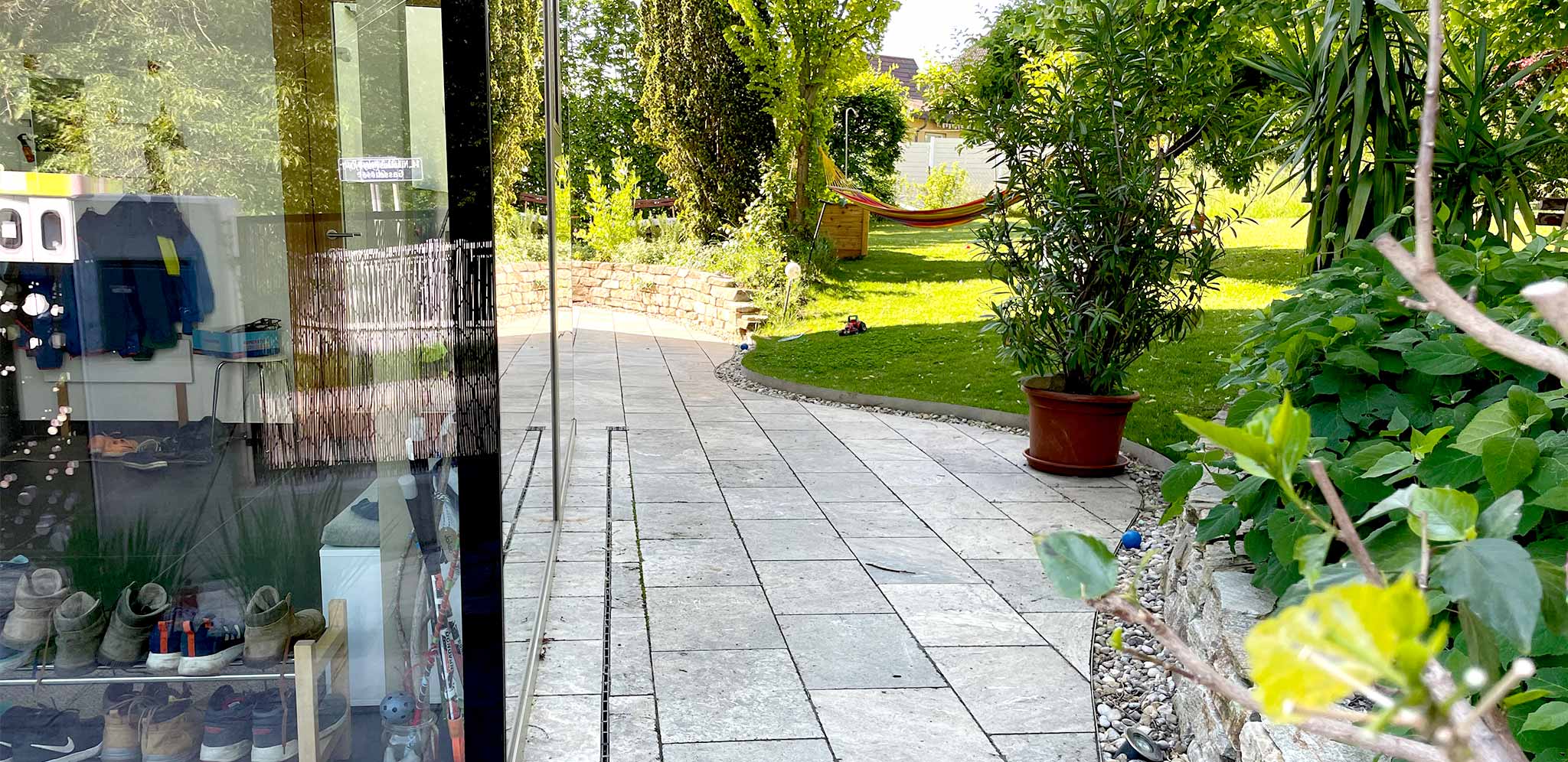 Gartenansicht auf einen üppigen Garten mit Steinterrasse und einer Hängematte im Hintergrund