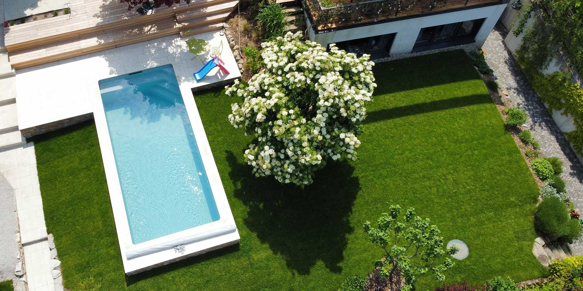 Eine Luftaufnahme zeigt einen großen Garten in Hanglage mit einem Pool und einer Holzterrasse mit Stiegen. Gartengestaltung in Wien und Umgebung